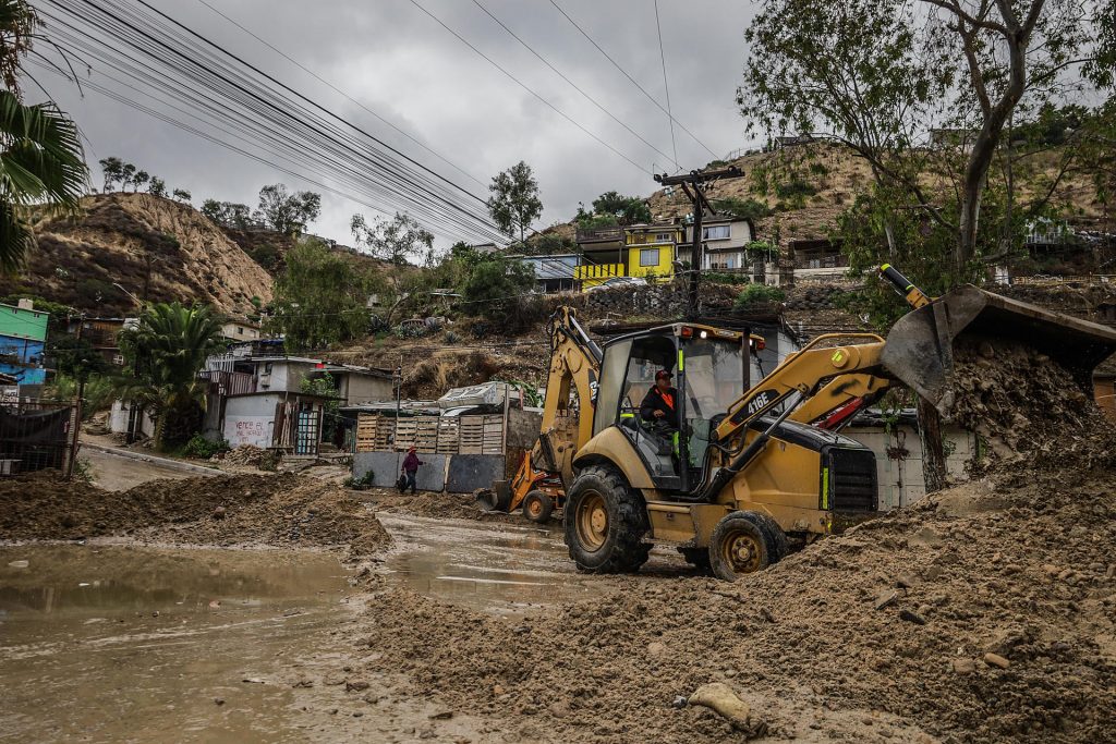 Un hombre trabaja con una maquina excavadora en una vía retirando lodo tras el paso de la tormenta Hilary en la ciudad de Tijuana (México).