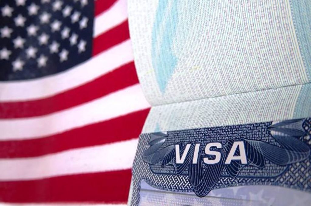 Visa americana con bandera de Estados Unidos de fondo.
