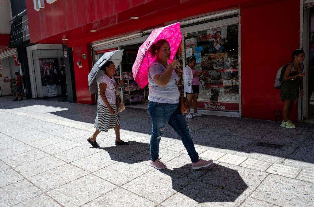 Mujeres caminando con sombrillas bajo altas temperaturas por ola de calor en México.